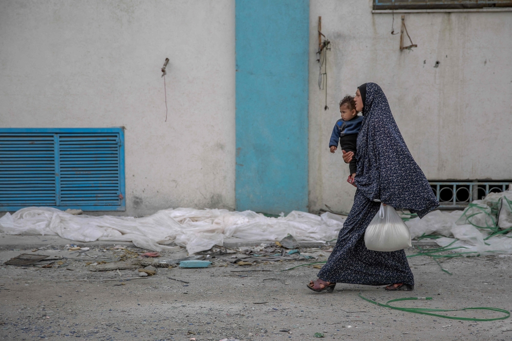 A woman carries her child and a bag of flour after humanitarian aid was distributed in Gaza City on March 17, 2024, amid ongoing battles between Israel and the Palestinian group Hamas. (Photo by AFP)
