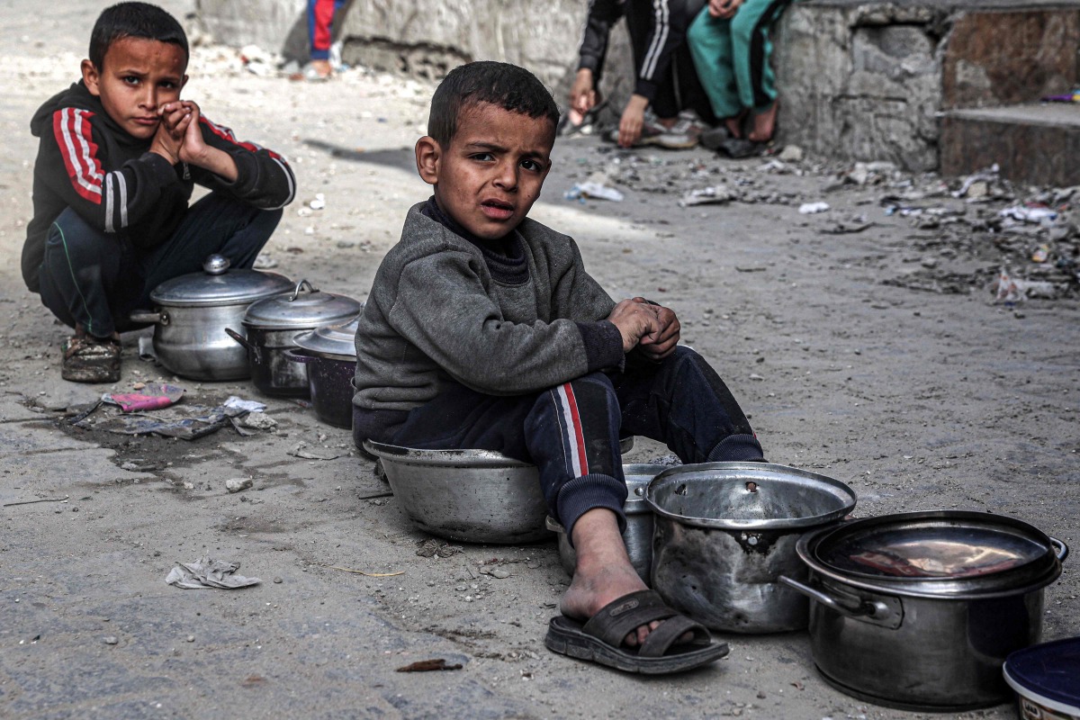 Boys sit with empty pots as displaced Palestinians queue for meals provided by a charity organisation ahead of the fast-breaking 