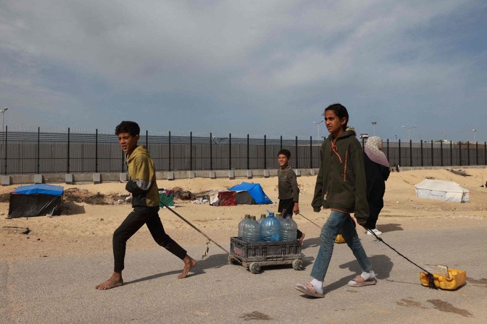 Palestinian children transport water to a camp for displaced people in Rafah in the southern Gaza Strip on March 17, 2024, amid ongoing battles between Israel and the militant group Hamas. (Photo by Mohammed Abed / AFP)