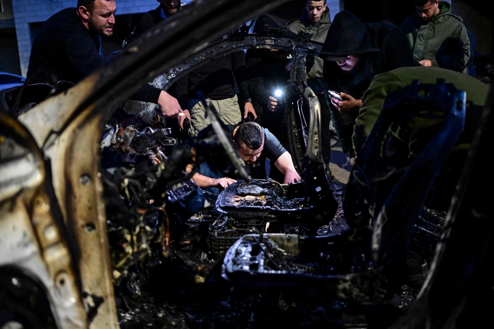 Palestinian men check a destroyed car following an Israeli air strike on Jenin in the occupied West Bank, on March 20, 2024. (Photo by RONALDO SCHEMIDT / AFP)
