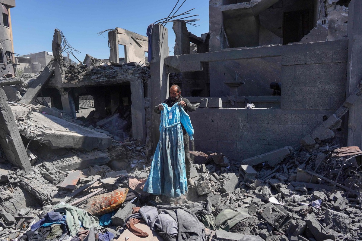 A Palestinian man picks a blue dress from the rubble following overnight Israeli bombardment which hit the al-Habash family home at the Nuseirat refugee camp in the central gaza Strip on March 20, 2024. (Photo by AFP)
