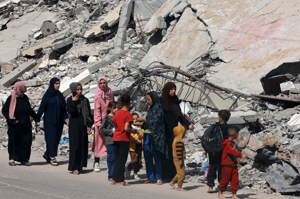 Palestinian women and children walk near a building destroyed in Israeli bombardment in Rafah in the southern Gaza Strip on March 31, 2024. (Photo by MOHAMMED ABED / AFP)
