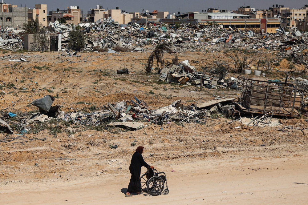 A Palestinian elderly woman pushes a wheelchair past rubble in Khan Yunis on April 7, 2024. (Photo by AFP)
