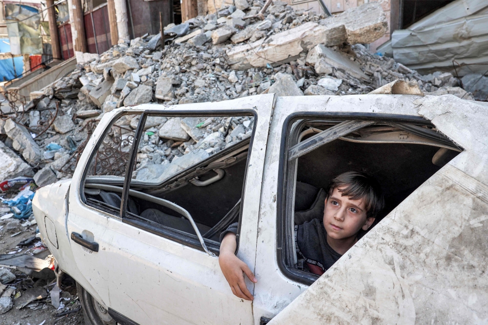 A boy looks out the window from inside a heavily damaged vehicle by the rubble of a collapsed building in Rafah in the southern Gaza Strip on April 9, 2024. (Photo by AFP)
 