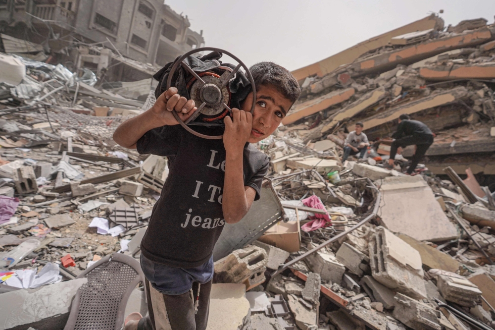 A Palestinian carries a gas cooker as he walks amidst the debris of a destroyed building in the city of Nuseirat in the central Gaza Strip on April 18, 2024.