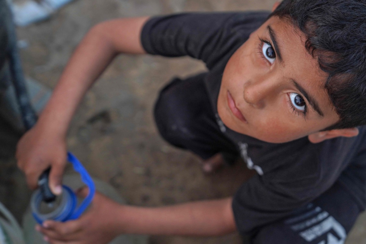 A Palestinian boy fills a canister with water from a hose in Deir el-Balah in the central gaza Strip on April 19, 2024. 