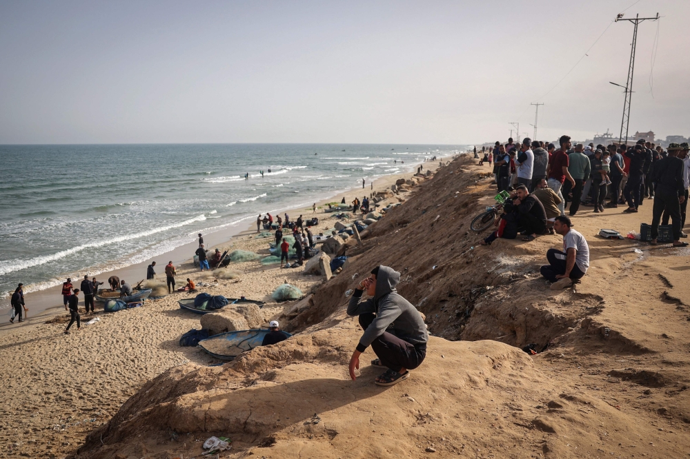 Palestinians watch fishermen returning at the beach next to a camp for the internally displaced in Rafah in the southern Gaza Strip on April 23, 2024. (Photo by AFP)
