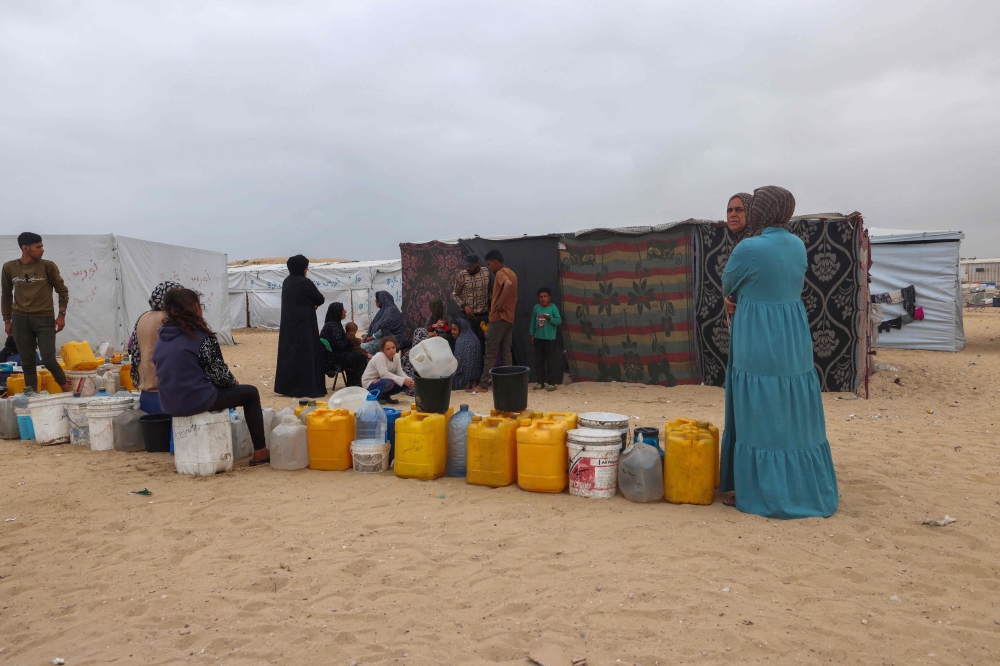 Displaced Palestinians wait by containers for water supply at their tent camp in Rafah in the southern Gaza Strip on April 26, 2024. Photo by MOHAMMED ABED / AFP