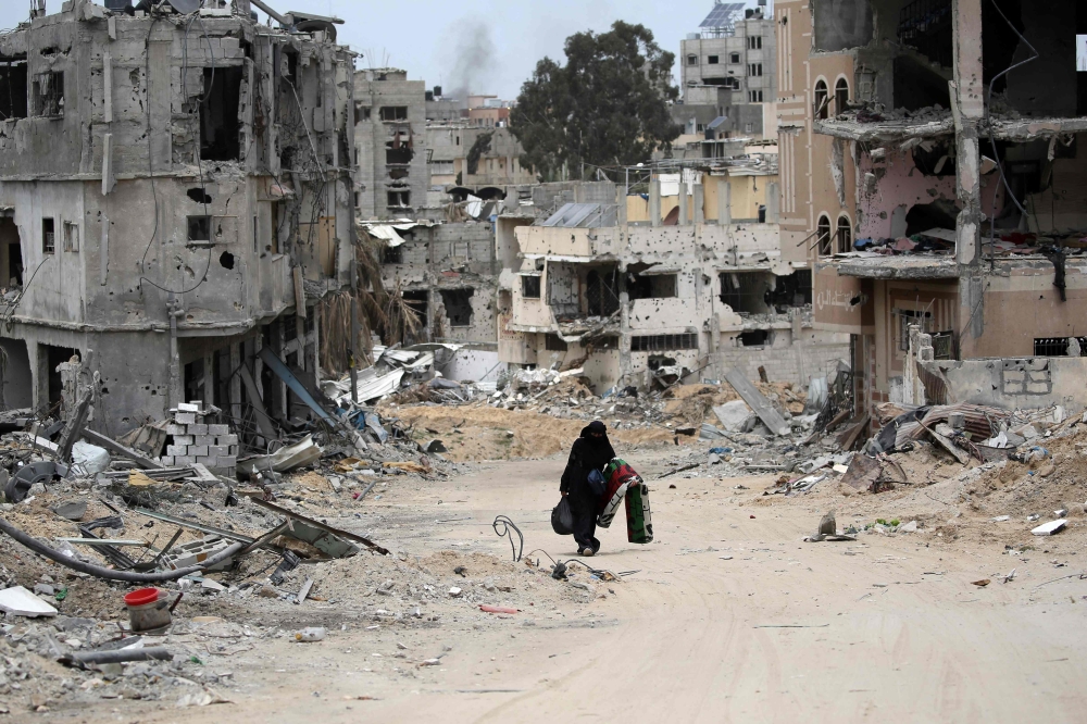 A Palestinian woman carrying some belongings walks in a neighbourhood devastated by Israeli bombing in Khan Yunis in the southern Gaza Strip on April 25, 2024. (Photo by AFP)
