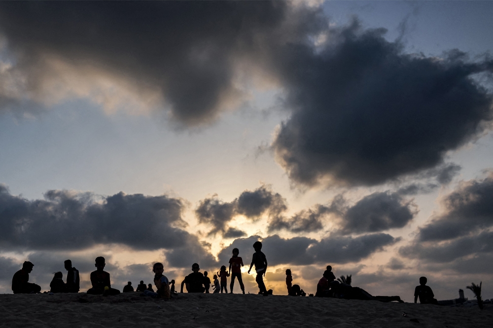 Clouds are pictured behind children at sunset at a camp housing displaced Palestinians in Rafah in the southern Gaza Strip on April 30, 2024. (Photo by AFP)
