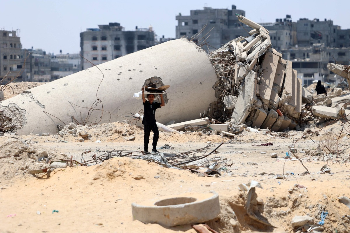 A Palestinian child transporting pieces of wood walks past a building destroyed by Israeli bombardment in Gaza City on May 3, 2024, amid the ongoing conflict between Israel and the militant group Hamas. (Photo by AFP)