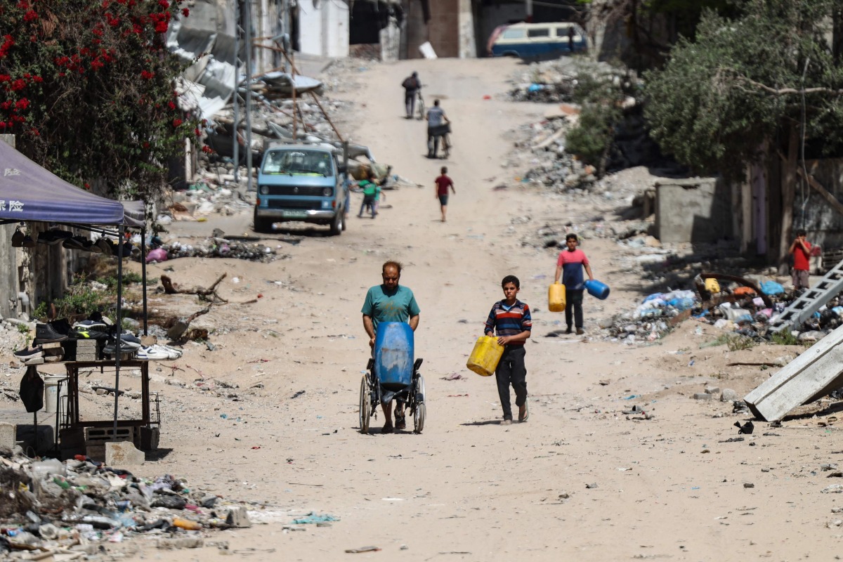 Palestinians carry recipients as they walk toward a water distribution point along a street devastated by Israeli bombardment in gaza City on May 3, 2024. (Photo by AFP)
