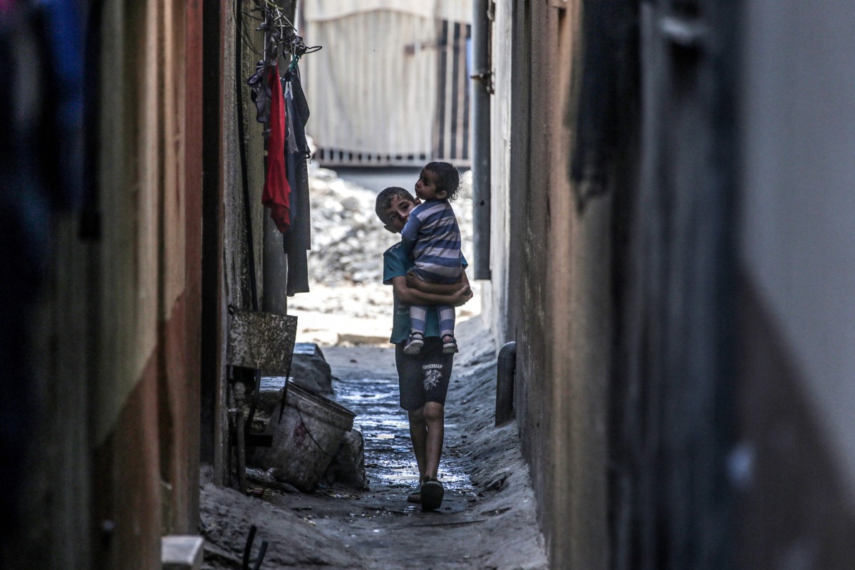 A Palestinian boy carries a toddler in an alley in Deir el-Balah in the central gaza Strip on May 15, 2024 . (Photo by AFP)