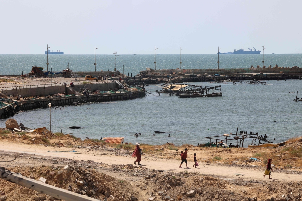 Palestinians walk past a jetty in Gaza City with a view of navy vessels off the coast as part of a humanitarian 