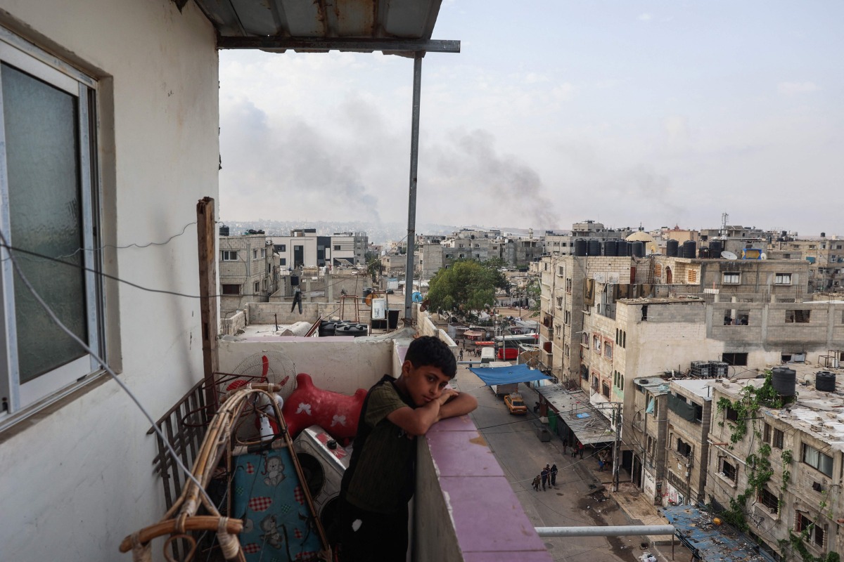 A boy stands on a balcony with a view of billowing smoke due to renewed Israeli strikes in Rafah city in the southern gaza Strip on May 28, 2024. (Photo by Eyad BABA / AFP) 