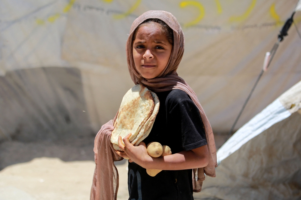 A Palestinian girl carries bread and potatoes at a camp for displaced people in Deir al-Balah in the central Gaza Strip on May 30, 2024. (Photo by Bashar Taleb / AFP)

