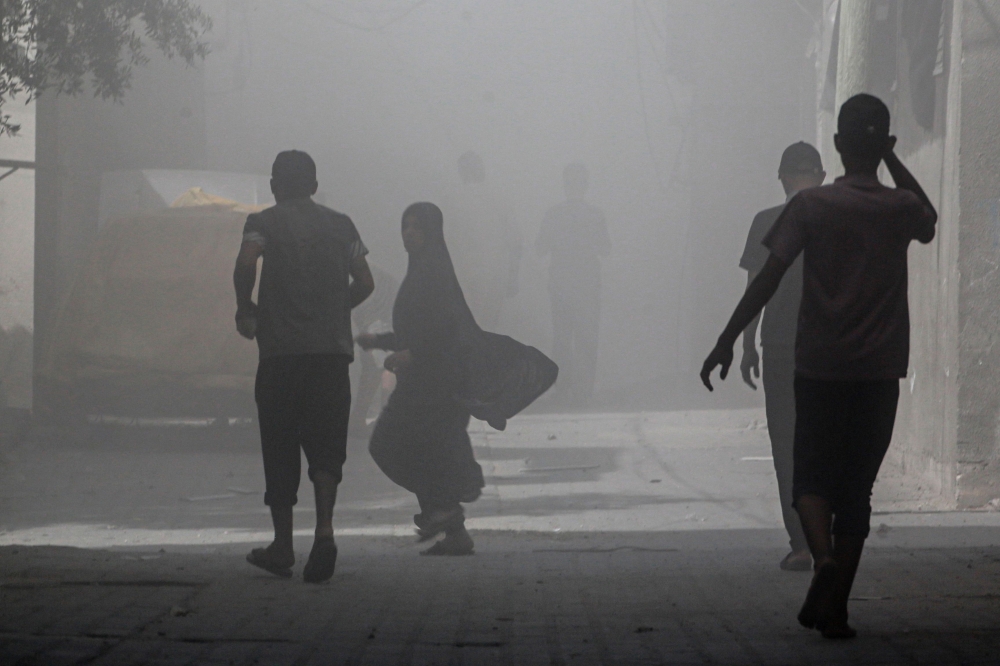 Palestinians walk through smoke and dust following an operation by the Israeli Special Forces in the Nuseirat camp, in the central Gaza Strip on June 8, 2024. (Photo by Bashar Taleb / AFP)