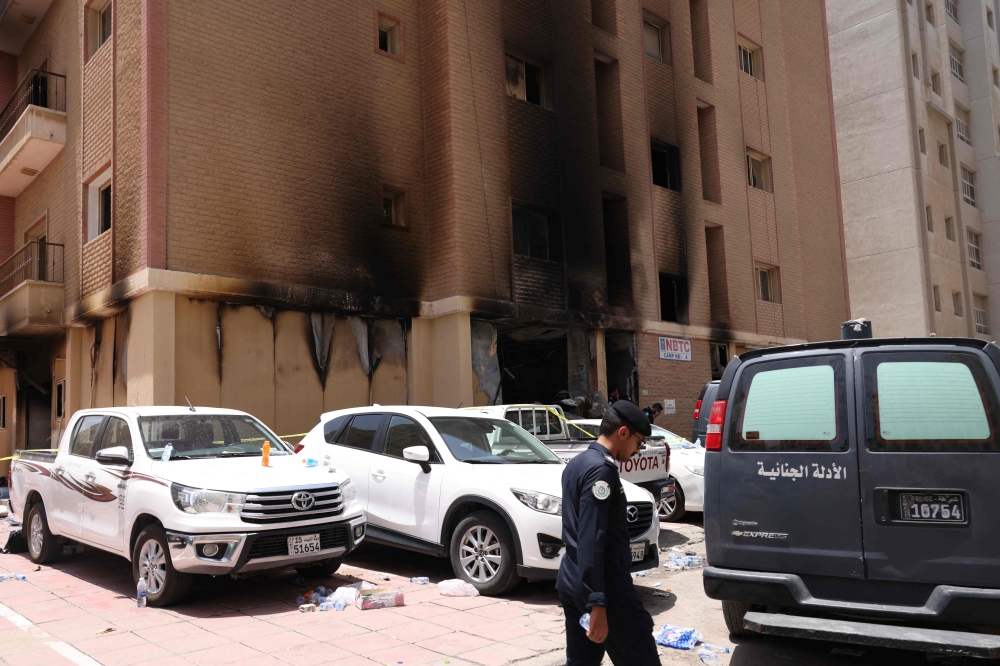 A member of the Kuwaiti security forces stand outside a building which was ingulfed by fire, in Kuwait City, on June 12, 2024. (Photo by Yasser Al-Zayyat / AFP)
