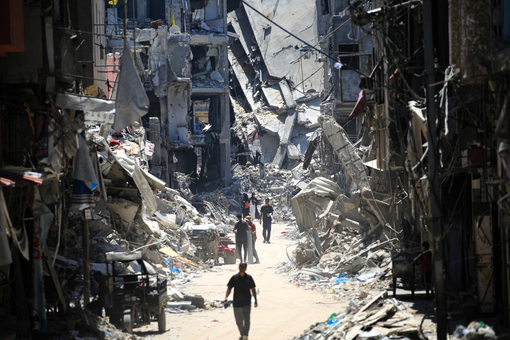 Palestinian men walk along a narrow street past destroyed buildings in Khan Yunis, in the southern Gaza Strip on June 11, 2024. Photo by Eyad BABA / AFP