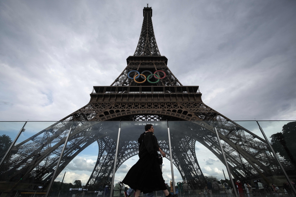 A person walk past the Eiffel Tower, decorated with the Olympic rings for the upcoming Paris 2024 Olympic Games, on June 14, 2024 in Paris. (Photo by Valentine Chapuis / AFP)