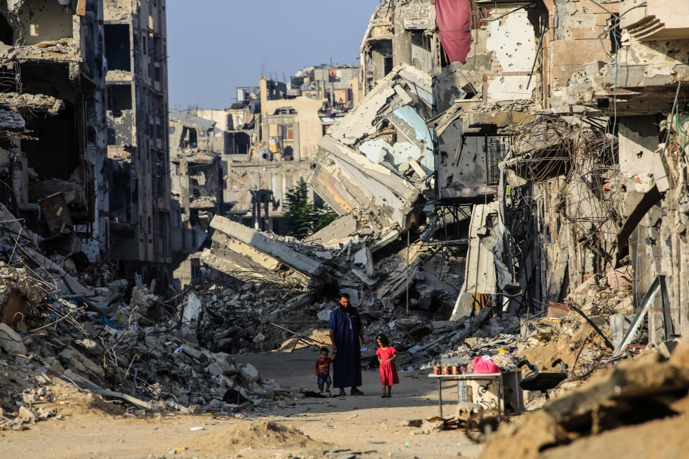 A man with his children walks past destroyed buildings in Khan Yunis on June 20, 2024. (Photo by Eyad Baba / AFP)