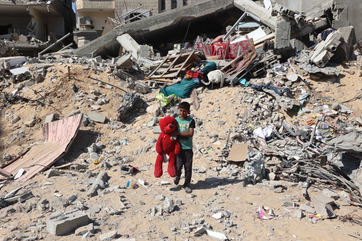 A Palestinian child walks with a stuffed bear recovered from the rubble of a destroyed building following Israeli bombardment in Khan Yunis on June 21, 2024, in the southern Gaza Strip. Photo by Eyad BABA / AFP.