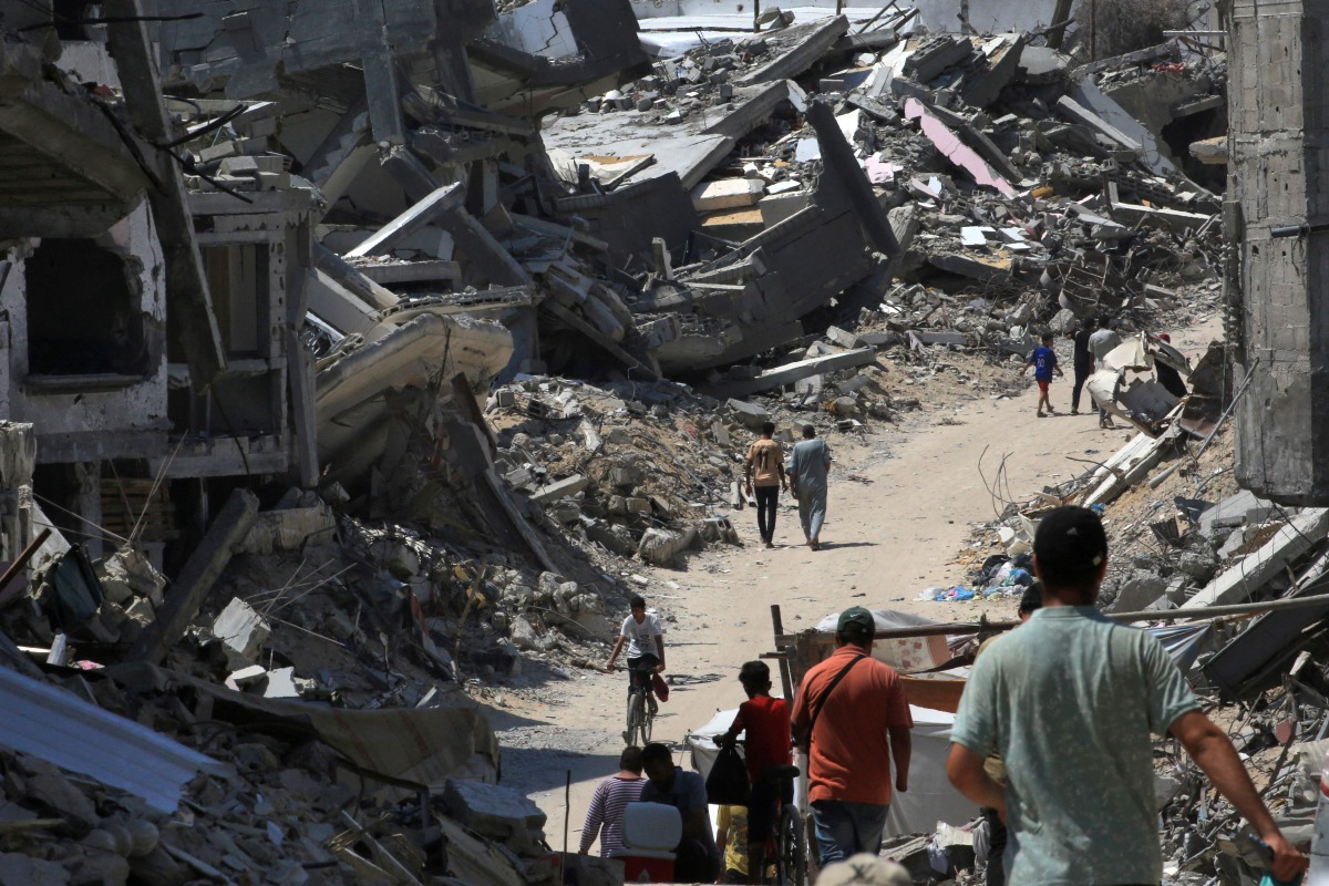 People walk along a road between the rubble of buildings destroyed during Israeli bombardment in Khan Yunis on the southern Gaza Strip on June 23, 2024. (Photo by Eyad BABA / AFP)