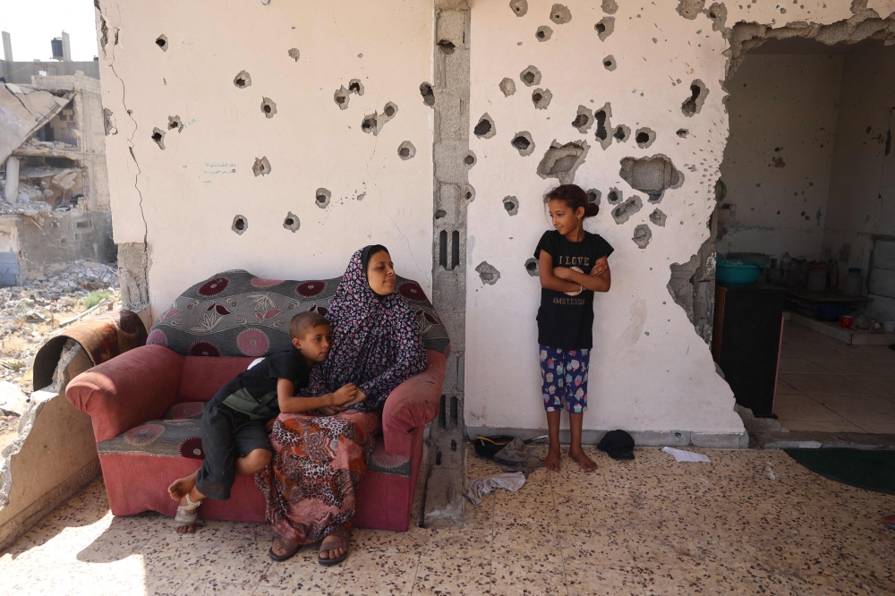 A Palestinian boy hugs a woman a she speaks to a girl while sitting on the balcony of a home damaged in previous Israeli bombardment, as some residents return to the city of Khan Yunis, in the southern Gaza Strip on June 30, 2024. (Photo by Eyad Baba / AFP)
