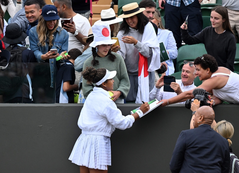 Japan's Naomi Osaka stands on a bench to sign autographs after winning against France's Diane Parry during their Women's singles tennis match on the first day of the 2024 Wimbledon Championships at The All England Lawn Tennis and Croquet Club in Wimbledon, southwest London, on July 1, 2024. (Photo by ANDREJ ISAKOVIC / AFP)
