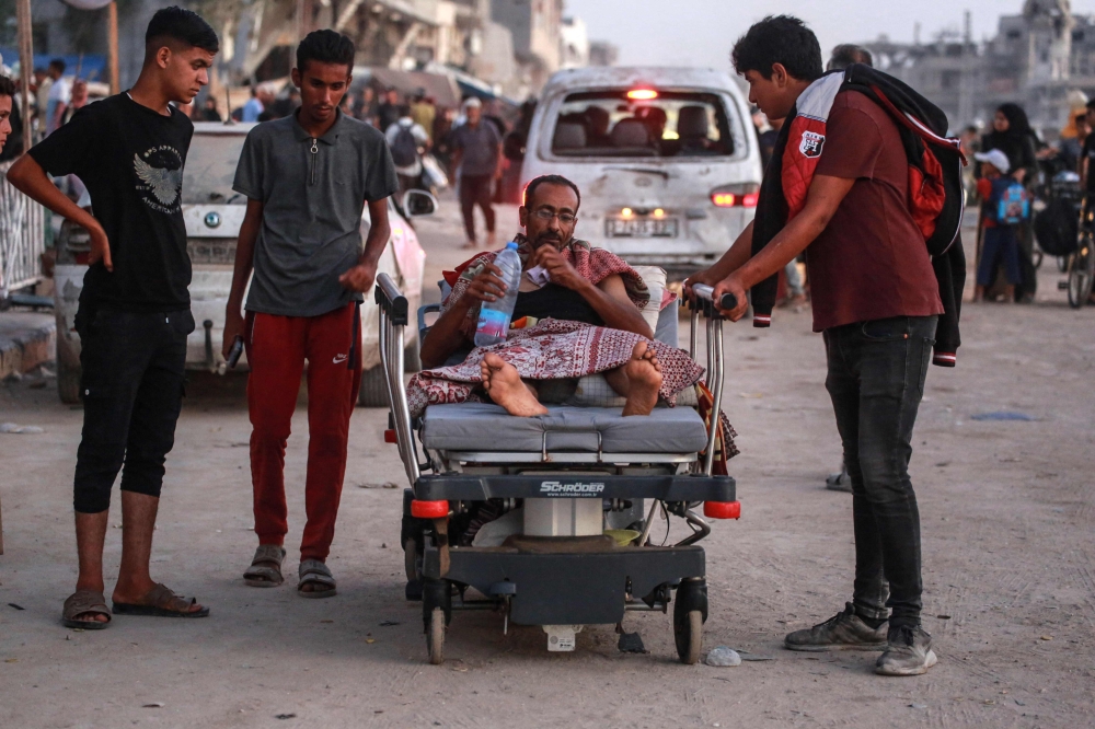 A man is transported on a hospital bed as displaced Palestinians leave an area in east Khan Yunis. (Photo by Bashar Taleb / AFP)