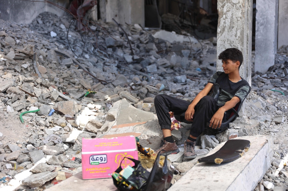 A Palestinian youth sits in the shade, on the remains of a chair placed on the rubble of buildings destroyed in previous Israeli bombardment, in the Sheikh Radwan neighbourhood, north of Gaza City on July 3, 2024. (Photo by Omar AL-QATTAA / AFP)
