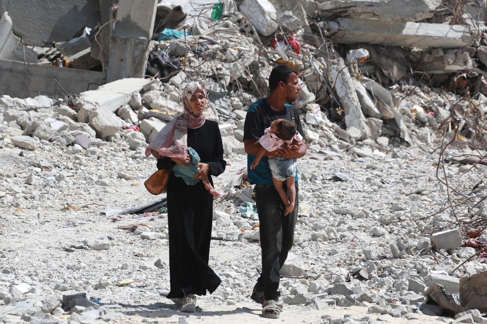 A Palestinian couple holds their children as they walk through debris in Khan Yunis in the southern Gaza Strip on July 4, 2024. (Photo by Bashar TALEB / AFP)
