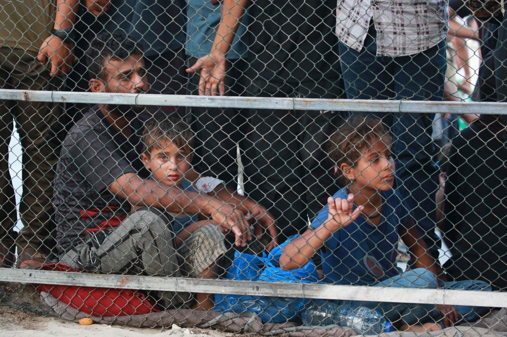 People sit behind a fence as they watch the arrival of victims wounded or killed in Israeli bombardment near Khan Yunis into Nasser hospital on July 9, 2024. (Photo by Bashar Taleb / AFP)