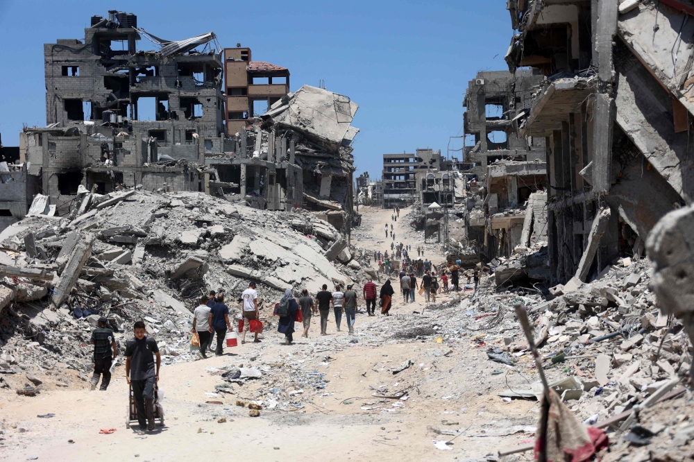 Palestinians make their way over the dirty of rubble, past destroyed buildings after the Israeli military withdrew following a two-week offensive from the Shujaiya neighbourhood, east of Gaza City on July 11, 2024. (Photo by Omar Al-Qattaa / AFP)