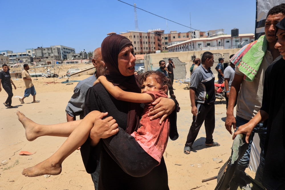 A Palestinian woman carries an injured child to the Nasser hospital in Khan Yunis on July 13, 2024. (Photo by Eyad Baba / AFP)
 