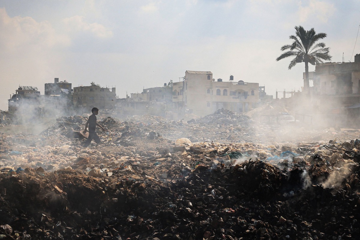  A Palestinian youth walks past piles of smouldering waste, as garbage collection and any other municipality services come to a halt due to the Israeli bombardment of the GAZA Strip, at the al-Maghazi Palestinian refugee camp, in the central GAZA Strip on July 15, 2024.(Photo by Eyad BABA / AFP)
