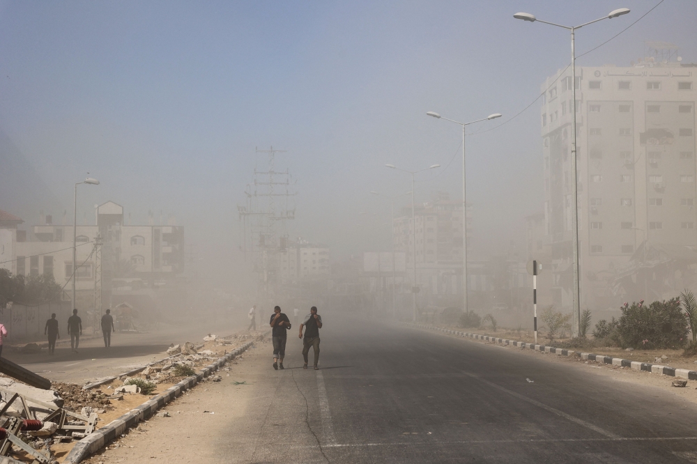 Palestinians walk away amid dust and smoke from the scene of an Israeli strike in Nuseirat in the central Gaza Strip on July 17, 2024. (Photo by Eyad Baba / AFP)