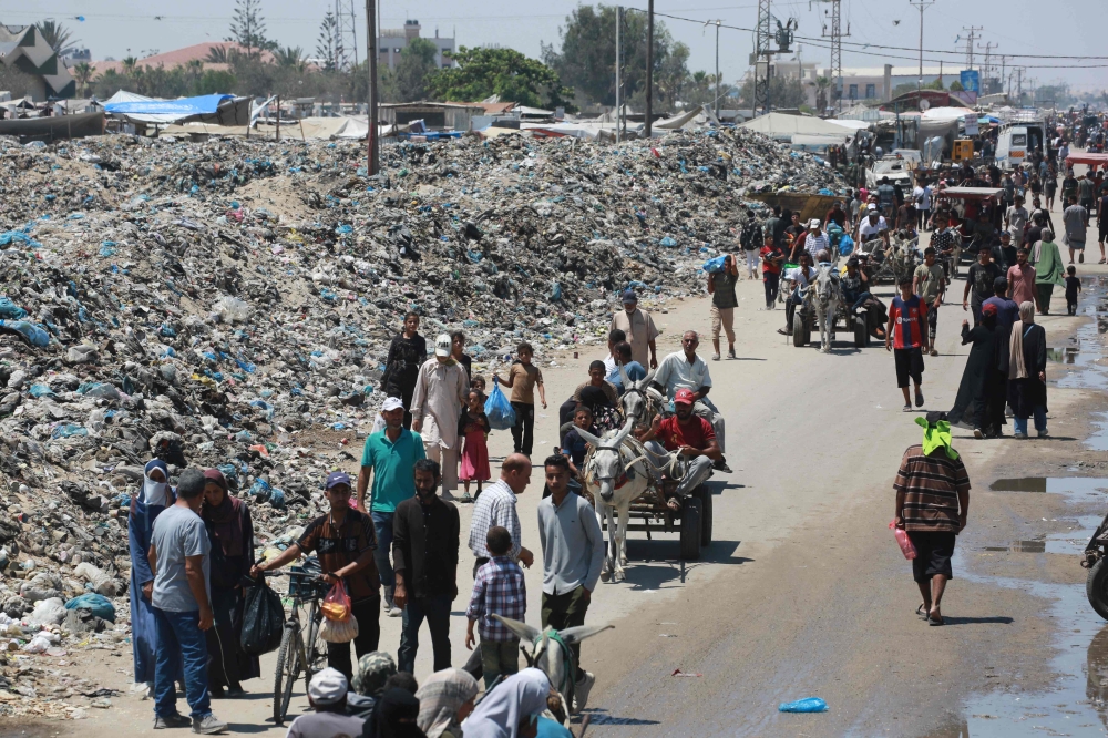 Palestinians walk past piles of garbage in Khan Yunis in the southern Gaza Strip on July 18, 2024. (Photo by Bashar Taleb / AFP)