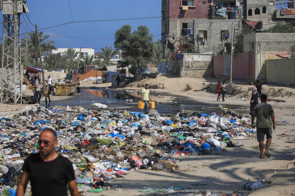 Palestinians walk past sewage water and a garbage dump on a street in Deir el-Balah in the central Gaza Strip on July 23, 2024. Photo by Eyad BABA / AFP