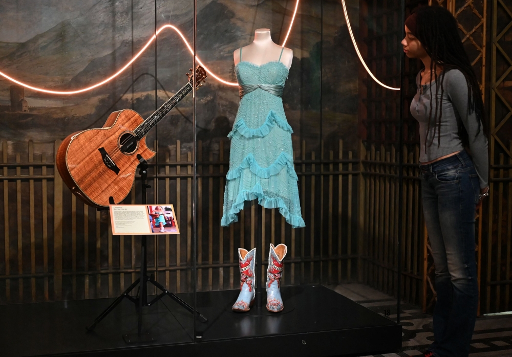 A gallery assistant looks at an ensemble worn by US artist Taylor Swift on her Soul2Soul II tour, with the dress designed by BCBG Max Azria, and the cowboy boots by Liberty Boot Co, during a photocall ahead of the forthcoming exhibition entitled 'Taylor Swift | Songbook Trail' at the V&A (Victoria and Albert) Museum in London on July 24, 2024. (Photo by Justin Tallis / AFP) 