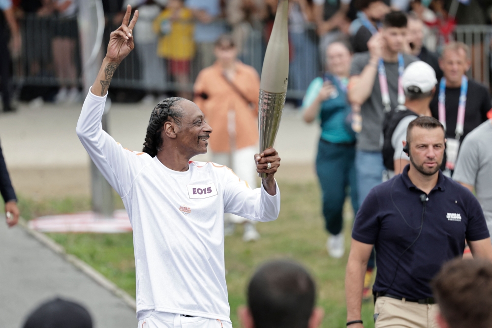 US rapper Snoop Dogg makes a peace sign as he holds the torch as part of the 2024 Paris Olympic Games Torch Relay, on the day of the opening ceremony, in Saint-Denis, outside Paris, on July 26, 2024. (Photo by STEPHANE DE SAKUTIN / AFP)