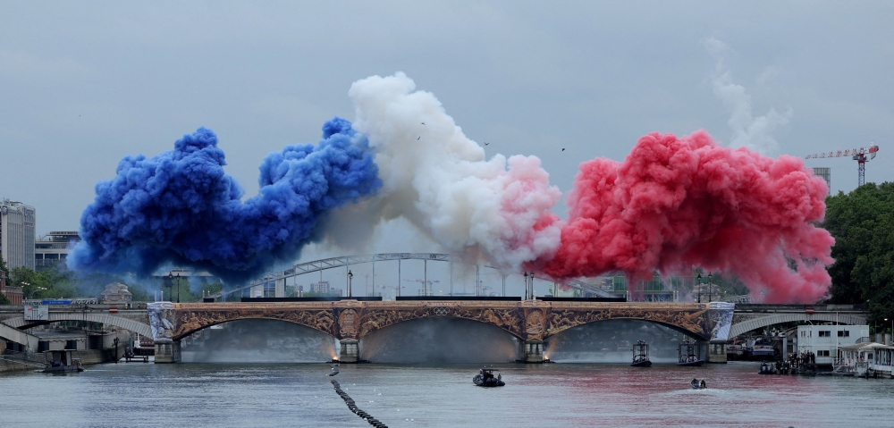 Coloured smoke forms the French flag on the Austerlitz bridge over the river Seine at the start of the opening ceremony of the Paris 2024 Olympic Games in Paris on July 26, 2024. (Photo by Ann Wang / POOL / AFP)