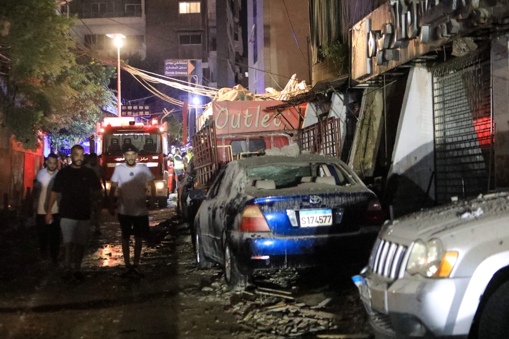 Men walk past debris after the top floors of an eight-storey building were destroyed following an Israeli military strike in a Beirut's southern suburb, on July 30, 2024. (Photo by AFP)
