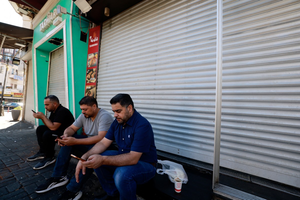 Palestinian men follow the news of the assassination of Hamas chief, Ismail Haniyeh in Iran, outside closed shops in central Ramallah in West Bank during a general strike on July 31, 2024. Photo by Jaafar ASHTIYEH / AFP