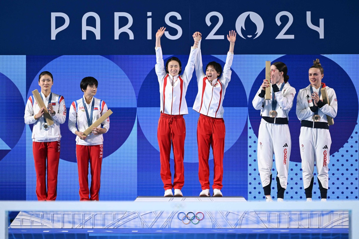 Silver medallists (L) North Korea's Jo Jin Mi and Kim Mi Rae, gold medallists (C) China's Chen Yuxi and Quan Hongchan and bronze medallists (R) Britain's Andrea Spendolini Sirieix and Lois Toulson celebrate on the podium following the women's synchronised 10m platform diving final at the Paris 2024 Olympic Games at the Aquatics Centre in Saint-Denis, north of Paris, on July 31, 2024. (Photo by SEBASTIEN BOZON / AFP)
