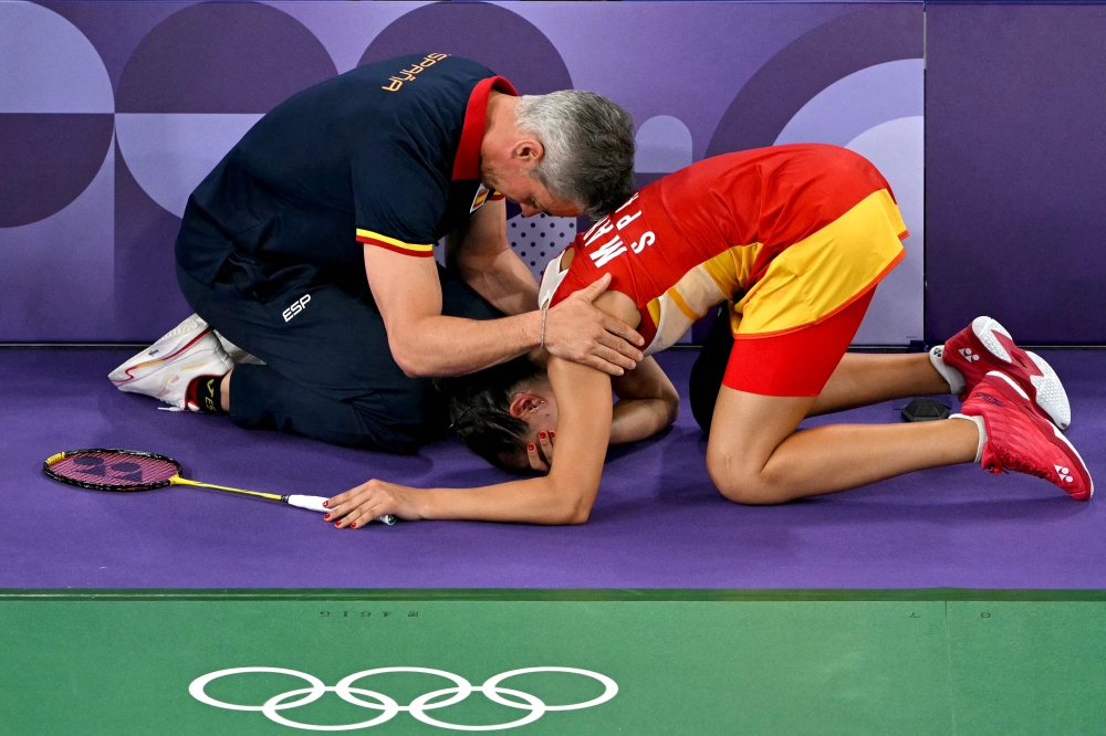 Spain's Carolina Marin is comforted by her coach Fernando Rivas as she concedes her women's singles badminton semi-final match against China's He Bing Jiao following an injury during the Paris 2024 Olympic Games at Porte de la Chapelle Arena in Paris on August 4, 2024. (Photo by Arun SANKAR / AFP)