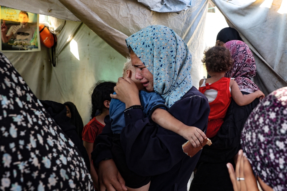 A woman carrying a child weeps following a reported overnight Israeli strike that hit tents used as temporary shelters by displaced Palestinians in the courtyard of the Al-Aqsa Martyrs hospital in Deir el-Balah in the central Gaza Strip, on August 4, 2024. (Photo by Eyad Baba / AFP)

