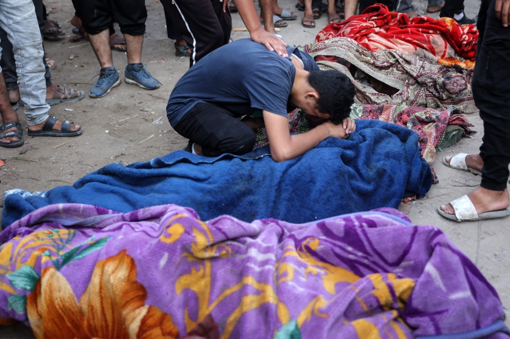 A young man mourns over the corpse of a person killed in an Israeli strike on a school used by displaced Palestinians as a temporary shelter in Gaza City on August 10, 2024, that killed more than 90 people. (Photo by Omar AL-QATTAA / AFP)