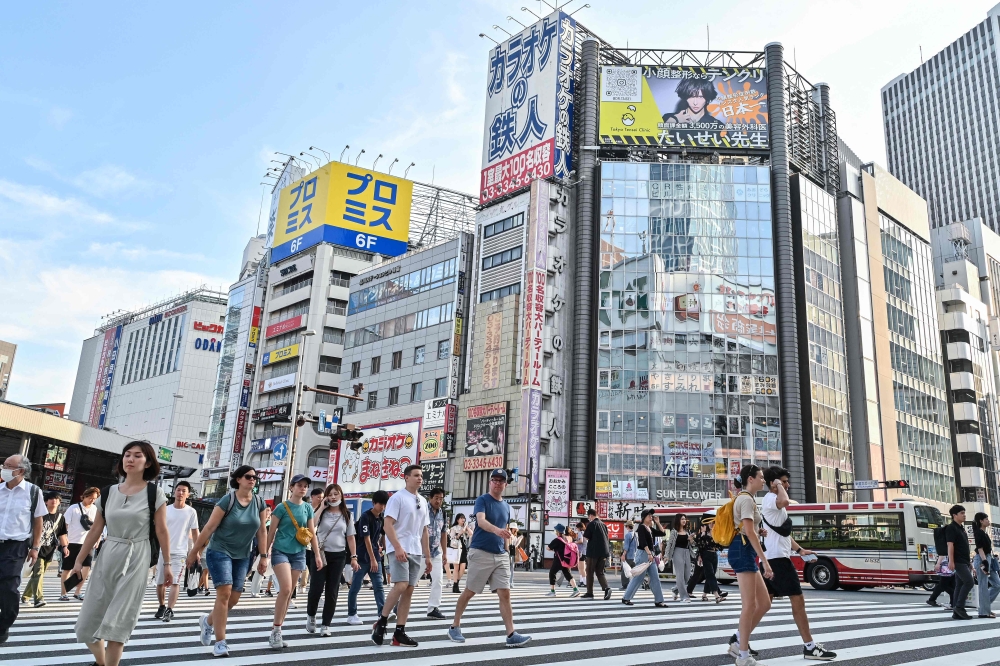 Pedestrians cross an intersection in the Shinjuku area of central Tokyo on August 13, 2024. (Photo by Richard A. Brooks / AFP)