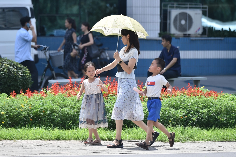 A woman uses an umbrella as she walks along the Mirae Scientists Street in Pyongyang during high temperatures on August 13, 2024. (Photo by KIM Won Jin / AFP)
